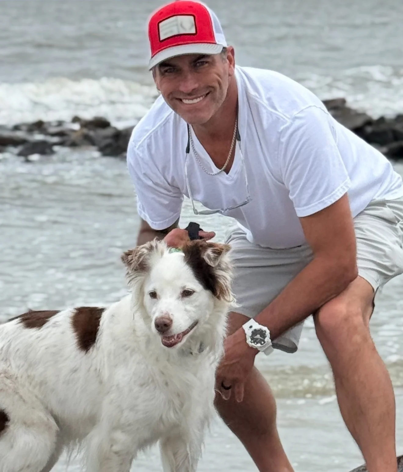 Barrett crouched on a beach beside Lola, a white and brown dog, with the surf behind them.